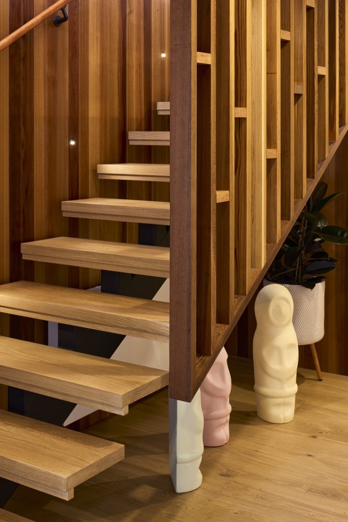 A wooden staircase with stained wood and 3 "Explorers" lolly inspired statuettes under the stairs.